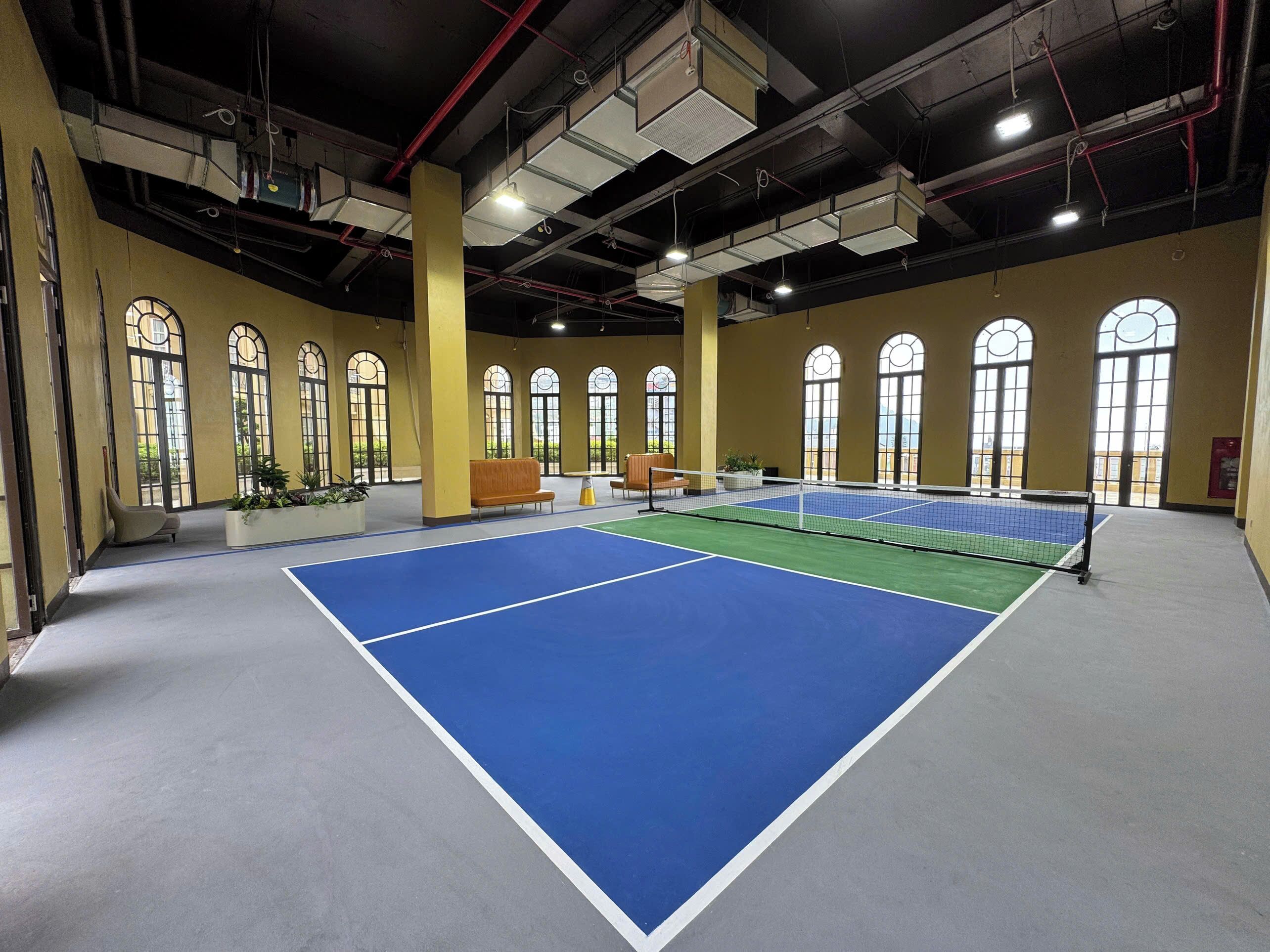 An indoor tennis court with seating and large windows.