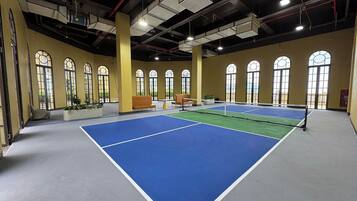 An indoor tennis court with seating and large windows.