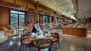 Ein geräumiger Hotel-Speisesaal mit mehreren gedeckten Tischen, großen Fenstern mit Ausblick und einer hohen, gewölbten Decke.