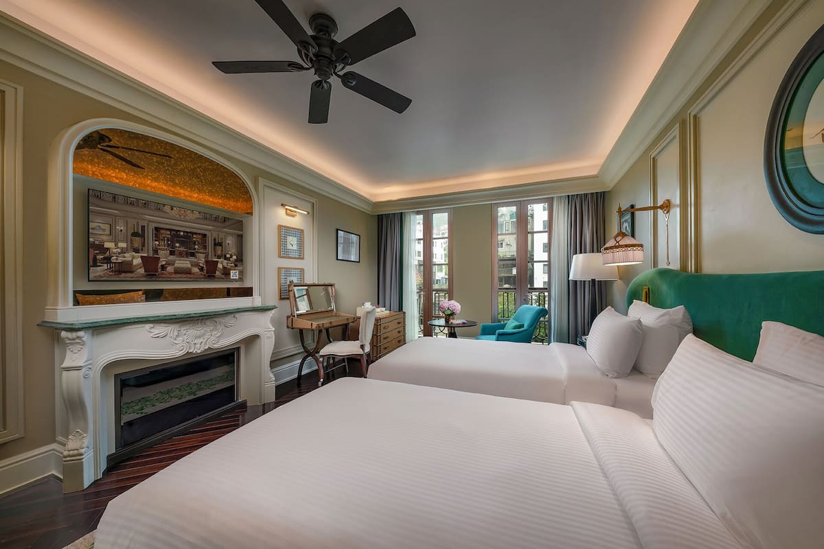 Habitación de hotel con una cama grande, chimenea, ventilador de techo y vistas al exterior a través de amplios ventanales.
