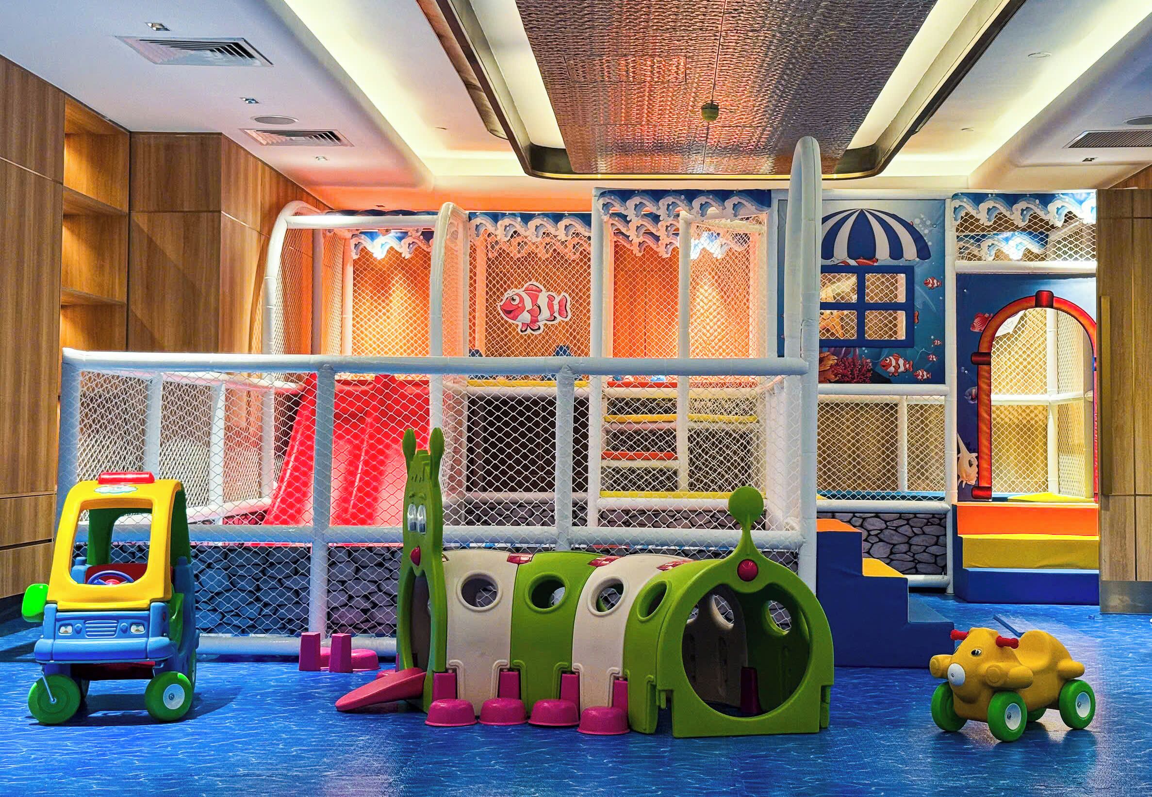 Zona infantil con una estructura de escalada, un tobogán y un pequeño vehículo.