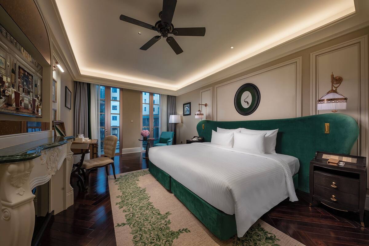 Un dormitorio amplio con una cama grande, un ventilador de techo y vistas de la ciudad a través de las ventanas.