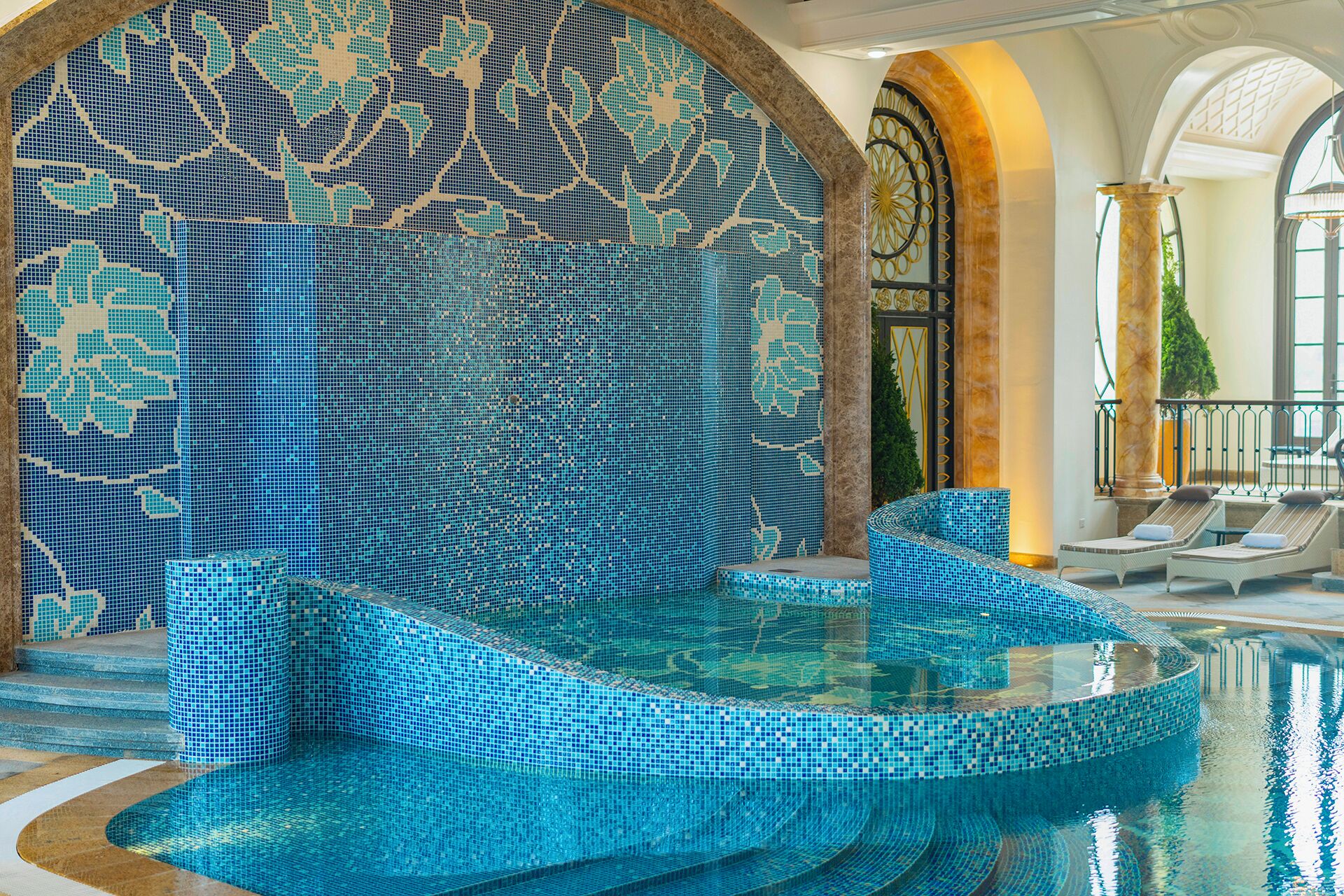 Un espace piscine avec des murs et des marches recouverts de mosaïques, qui permettent d’accéder à l’eau.