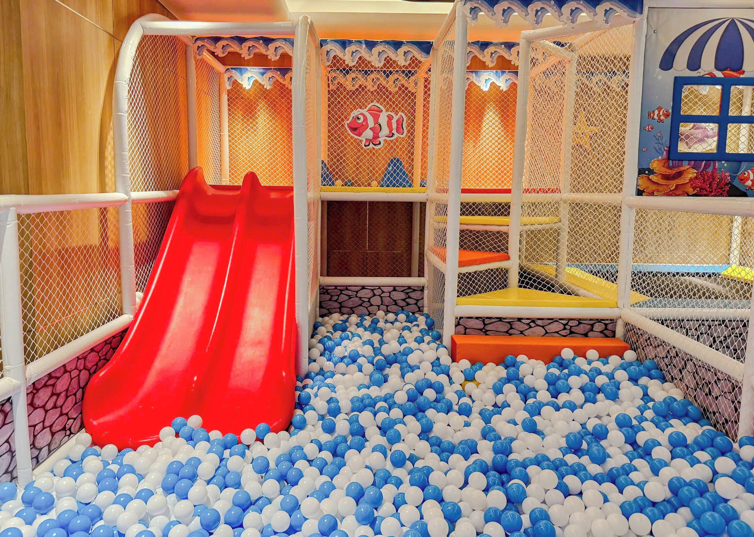Ein Spielbereich mit einer roten Rutsche und einem Ballbecken voller blauer und weißer Bälle.