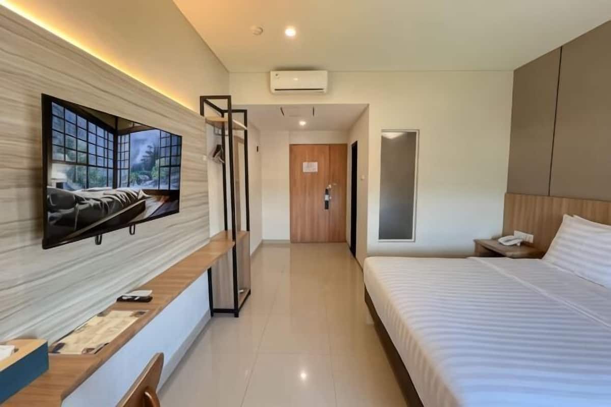 A modern hotel room with a bed, a desk, a chair, a TV mounted on the wall, and a door leading to another room.