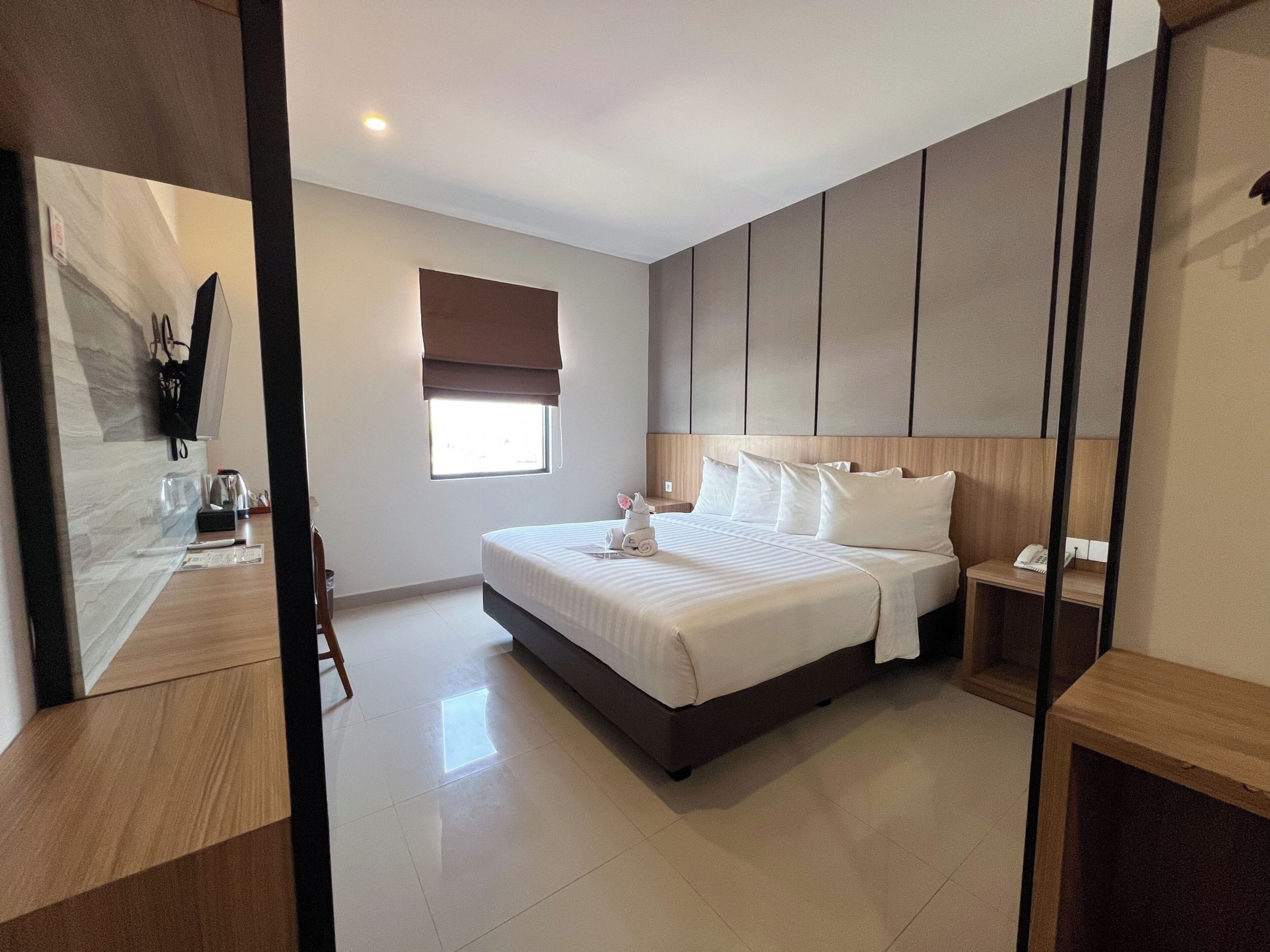A modern hotel room with a large bed, bedside tables, a window with a view, and a wooden floor.