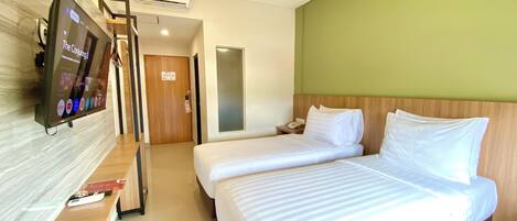 A hotel room with two beds, a TV on the wall, a wooden headboard, and a green accent wall.