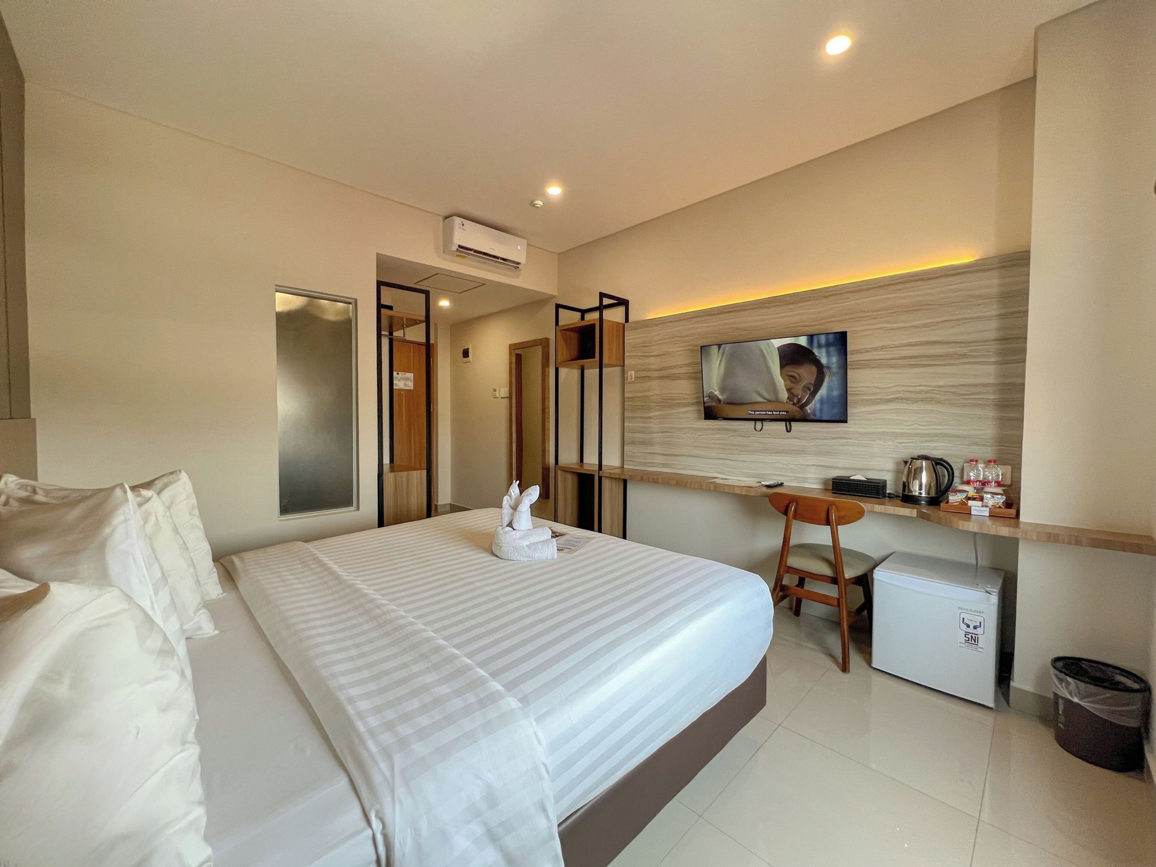 A hotel room with a bed, a desk, a television, a mini-fridge, and a trash bin.