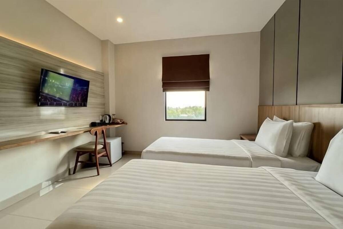 A modern hotel room with two beds, a TV mounted on the wall, a desk, and a window with a view.