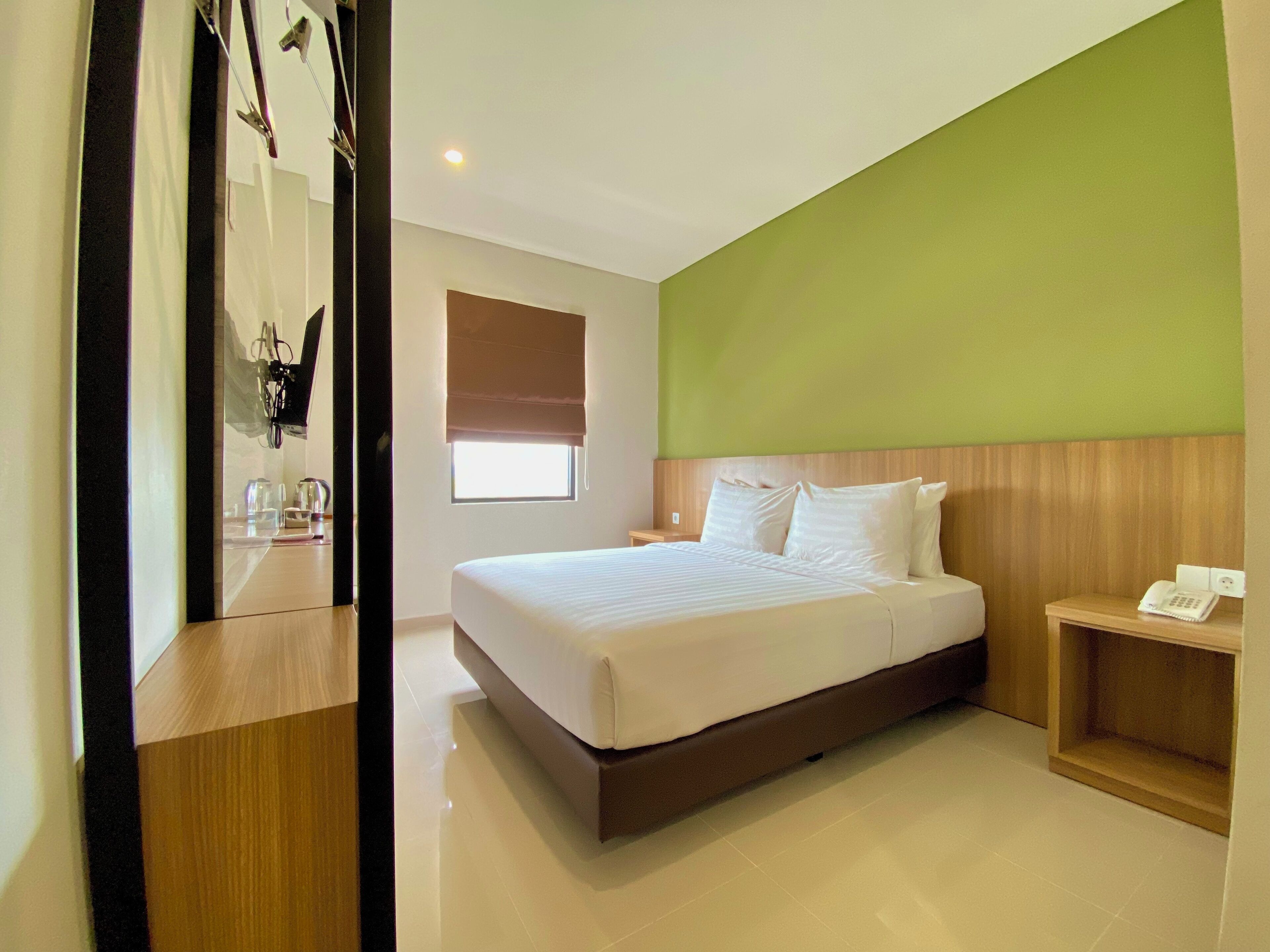 Habitación de hotel con una cama grande, cabecera de madera, mesita de noche con teléfono y ventana con persianas.