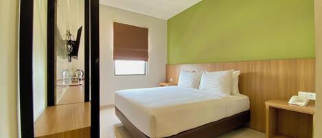 Habitación de hotel con una cama grande, cabecera de madera, mesita de noche con teléfono y ventana con persianas.