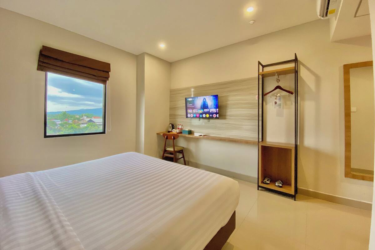A hotel room with a bed, a desk, a TV, and a wardrobe.