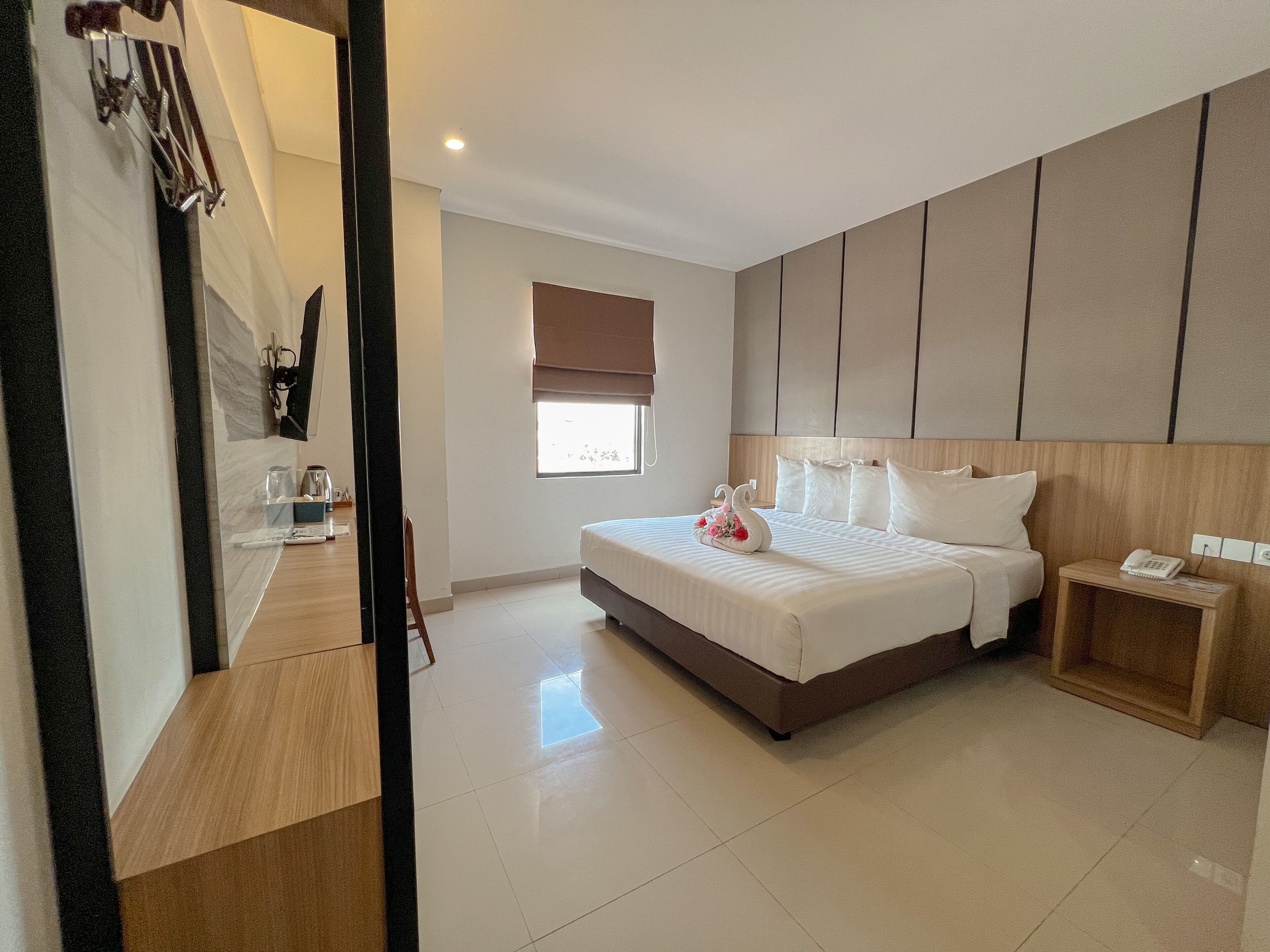A hotel room with a large bed, bedside tables, a window with blinds, and a wooden headboard.