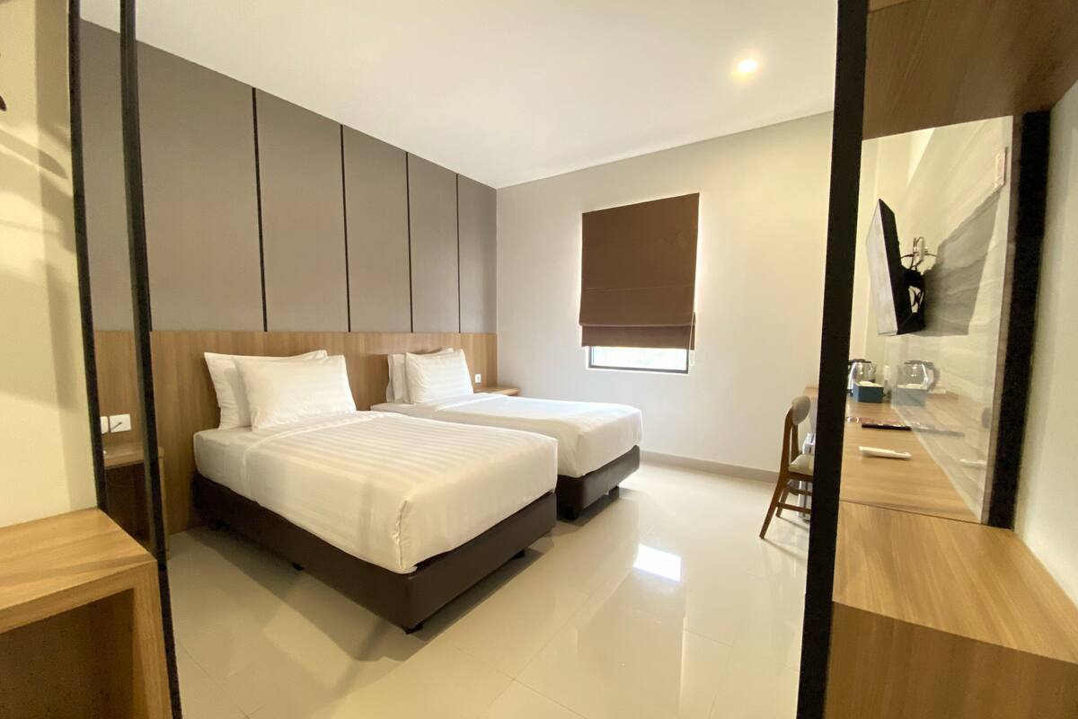 A modern hotel room with two beds, a small desk, and a large mirror.