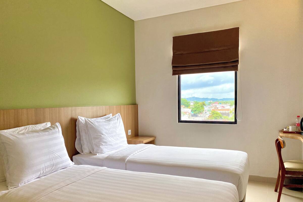 A hotel room with two beds, a window with a view, and a small wooden table with a chair.