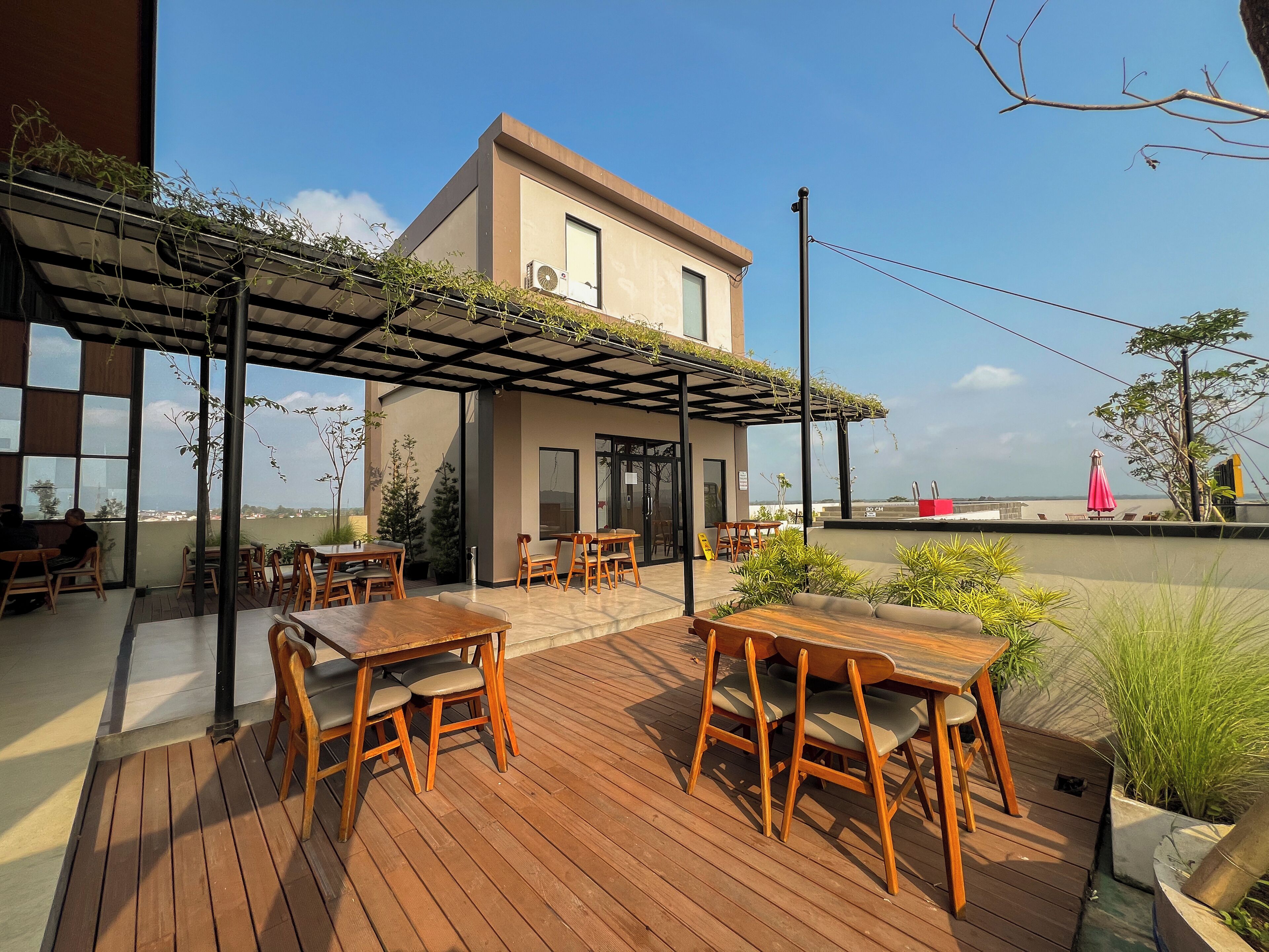 Une terrasse sur le toit, avec des tables et des chaises en bois, une pergola couverte de plantes grimpantes et une vue sur le paysage urbain.