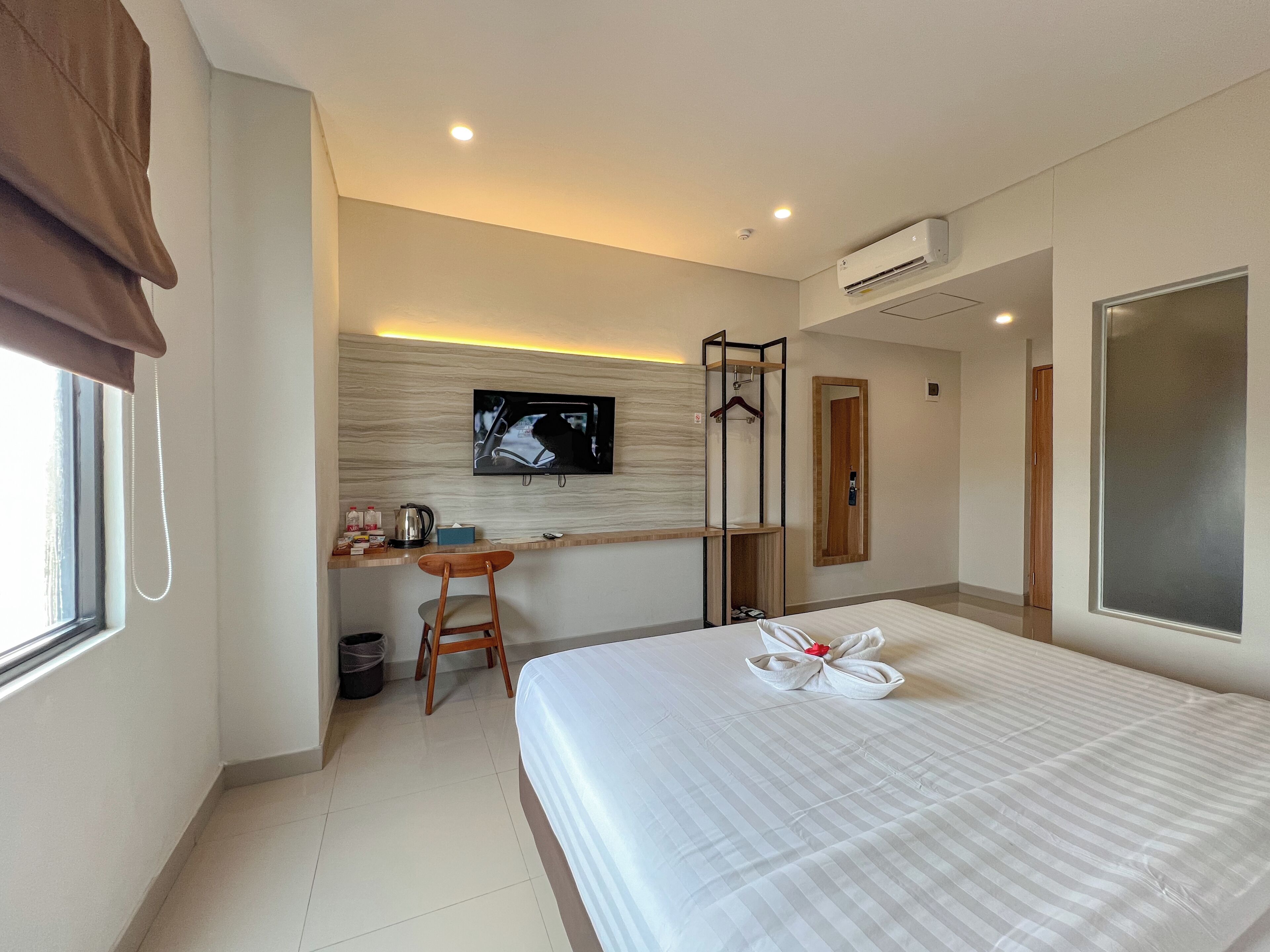 A hotel room with a bed, a desk with a chair, a television, and an air conditioning unit.
