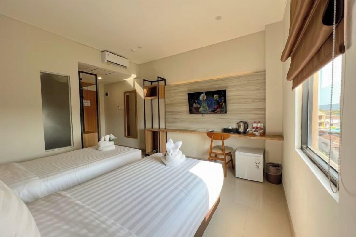 A hotel room with two beds, a small kitchenette, a desk, and a large window.
