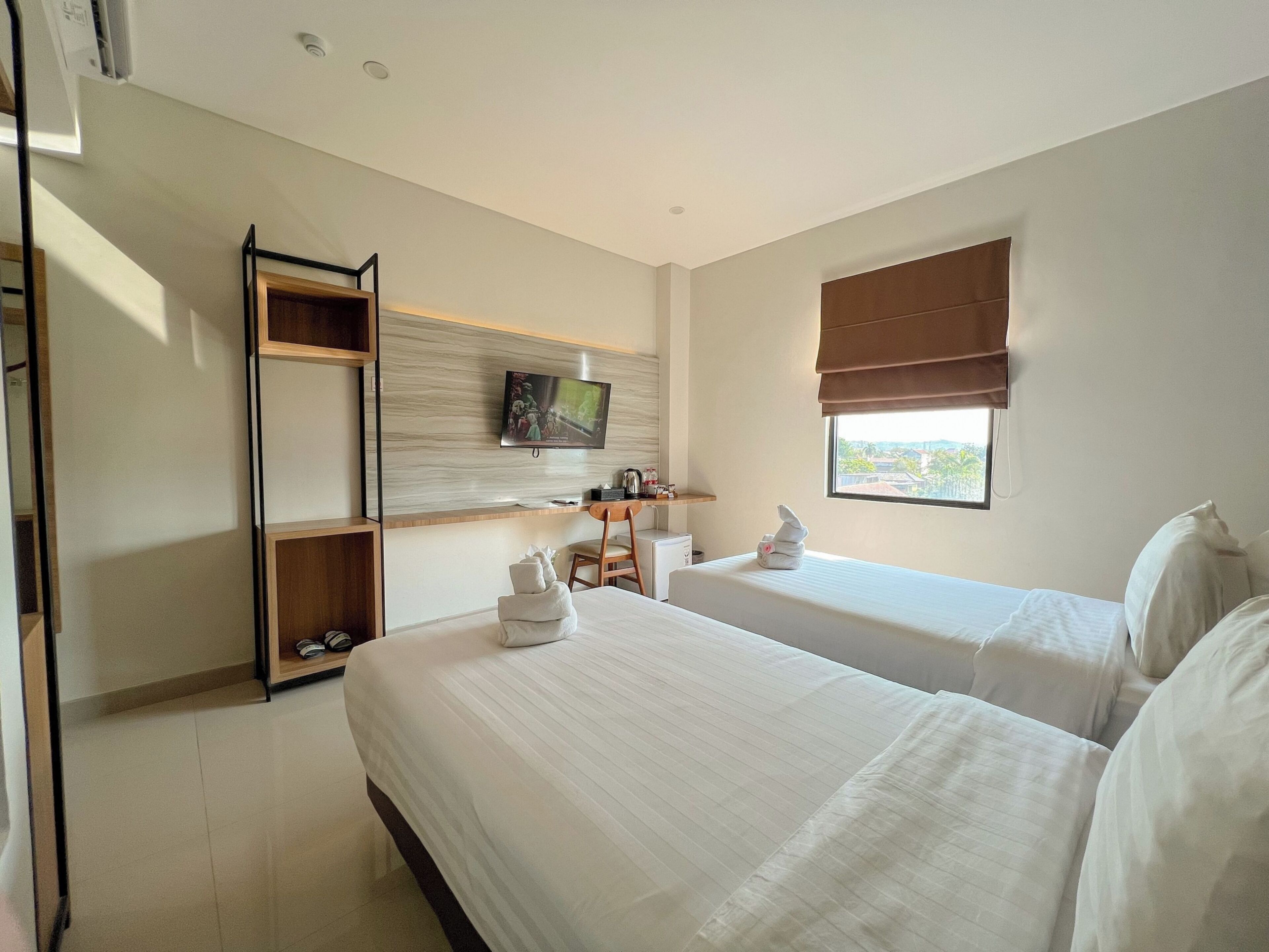 A hotel room with two beds, a desk, a television, and a window with a view.