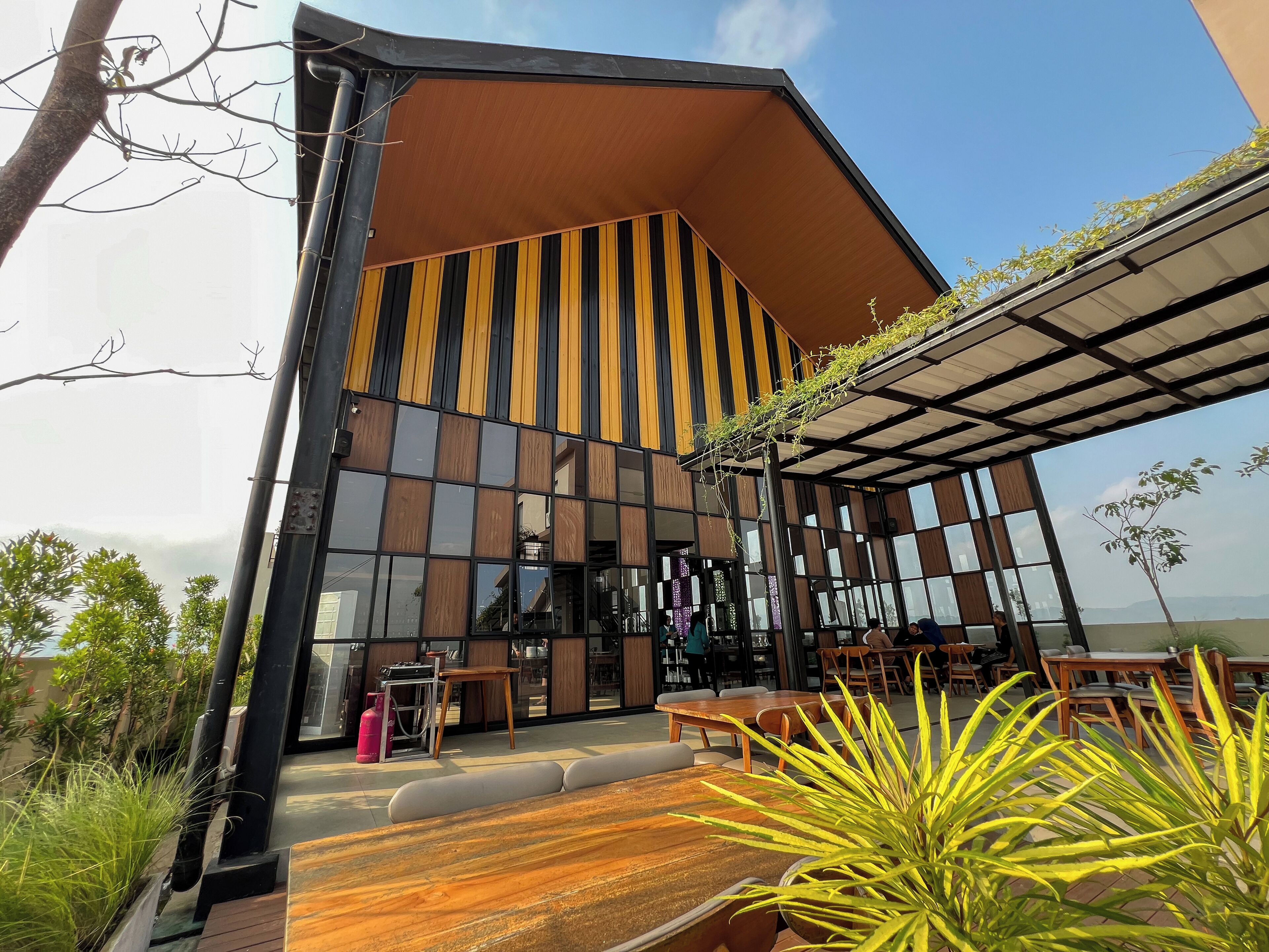 A modern building with a sloped roof and large windows. There are outdoor seating areas with tables and chairs.