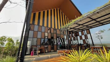 A modern building with a sloped roof and large windows. There are outdoor seating areas with tables and chairs.