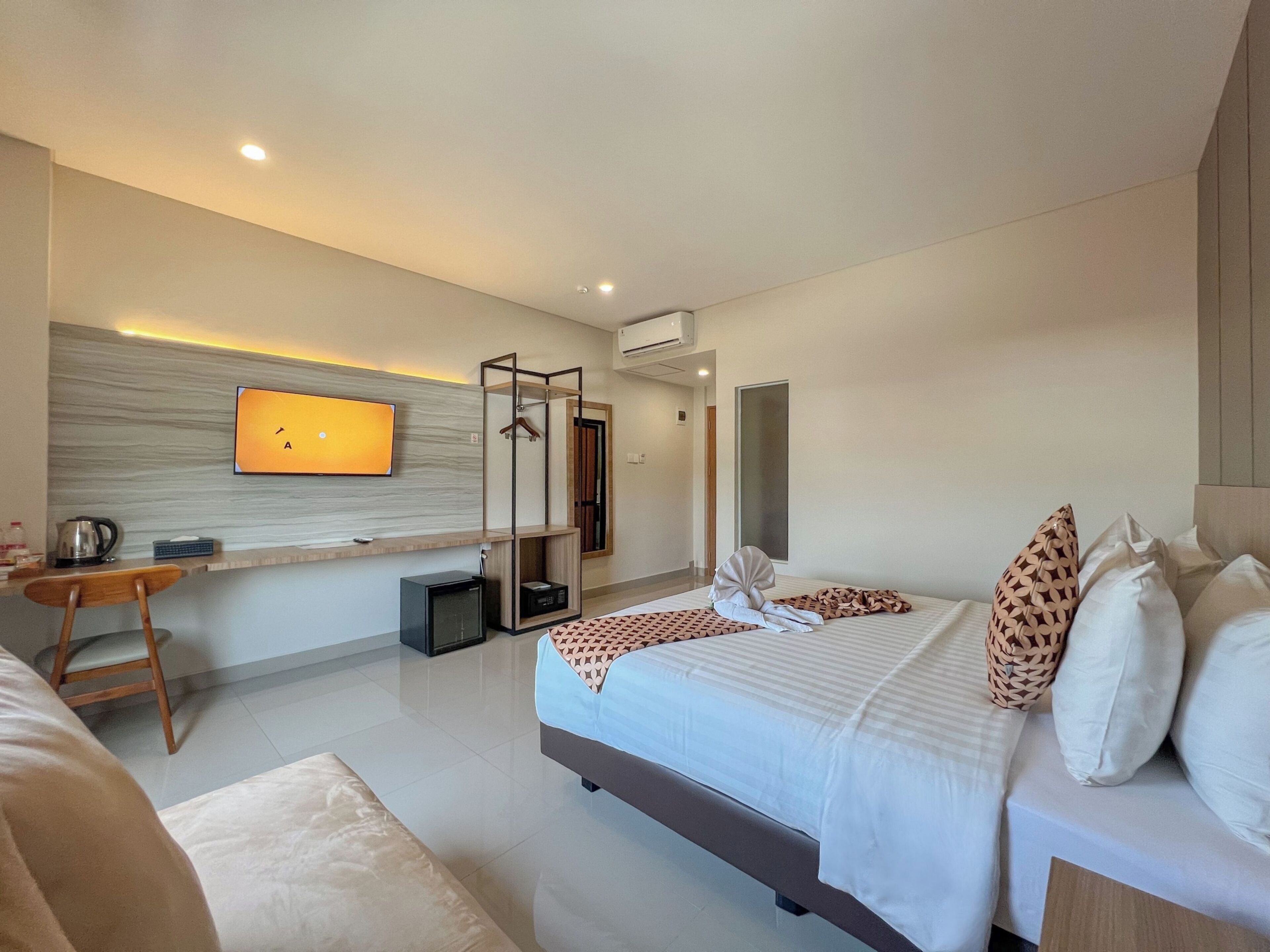 A modern hotel room with a bed, a desk, a television, and a mirror.