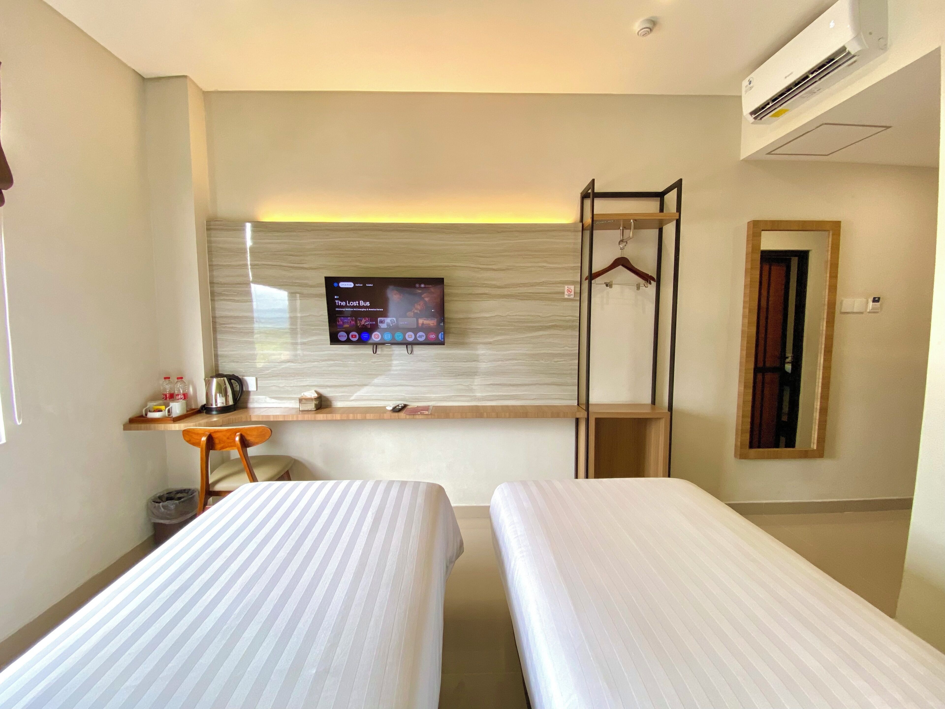 A hotel room with two beds, a TV mounted on the wall, a desk with a chair, and a mirror.