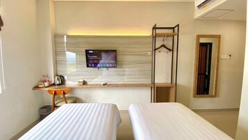 A hotel room with two beds, a TV mounted on the wall, a desk with a chair, and a mirror.