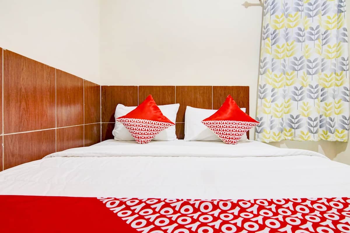 A bed with a white and red patterned bedspread, two red and white pillows, and a wooden headboard.