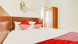 Une chambre d’hôtel avec une tête de lit en bois, un lit avec une literie blanche et rouge, et une décoration murale représentant un vélo et une citation.
