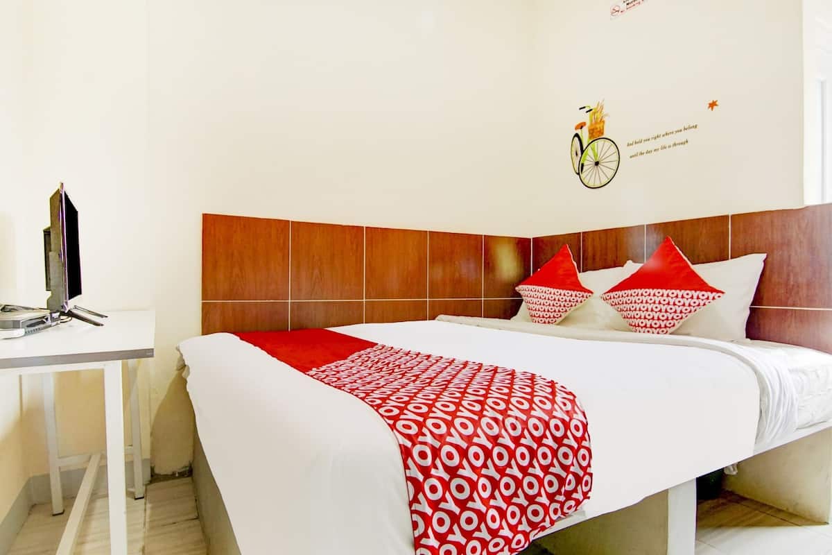 A hotel room with a wooden headboard, a bed with white and red bedding, and a wall decoration of a bicycle and text.