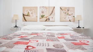 Un dormitorio con cama, almohadas blancas, colcha y tres cuadros de flores colgados en la pared.