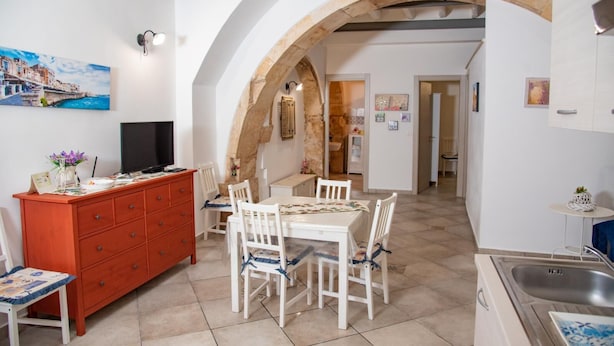Una cocina acogedora con comedor, que presenta un arco de piedra, muebles blancos y un televisor sobre un aparador.