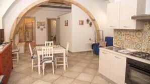 Una cocina con un arco, armarios blancos, una estufa a gas y un comedor con mesa y sillas.