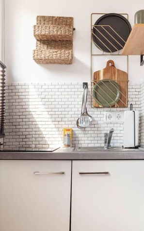 Una cocina con armarios blancos, salpicadero de ladrillo y diferentes utensilios y electrodomésticos.