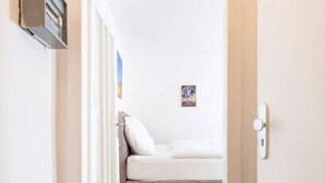 A narrow hallway leading to a bedroom with a bed and a small picture on the wall. - City Apartment in Berühmter Lage (Hildesheim)