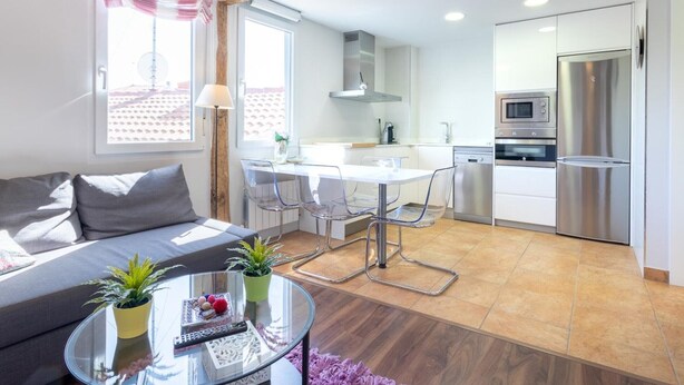 A modern living room with a glass coffee table, a sofa, and a dining area with chairs and a table. There is a kitchen with a refrigerator, microwave, and oven. - Bright apartment in Mundaka, perfect for couples and families, near the beach (Mundaca)