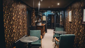 Un coin bar à la lumière tamisée, avec des chaises recouvertes d’un tissu vert et un comptoir.