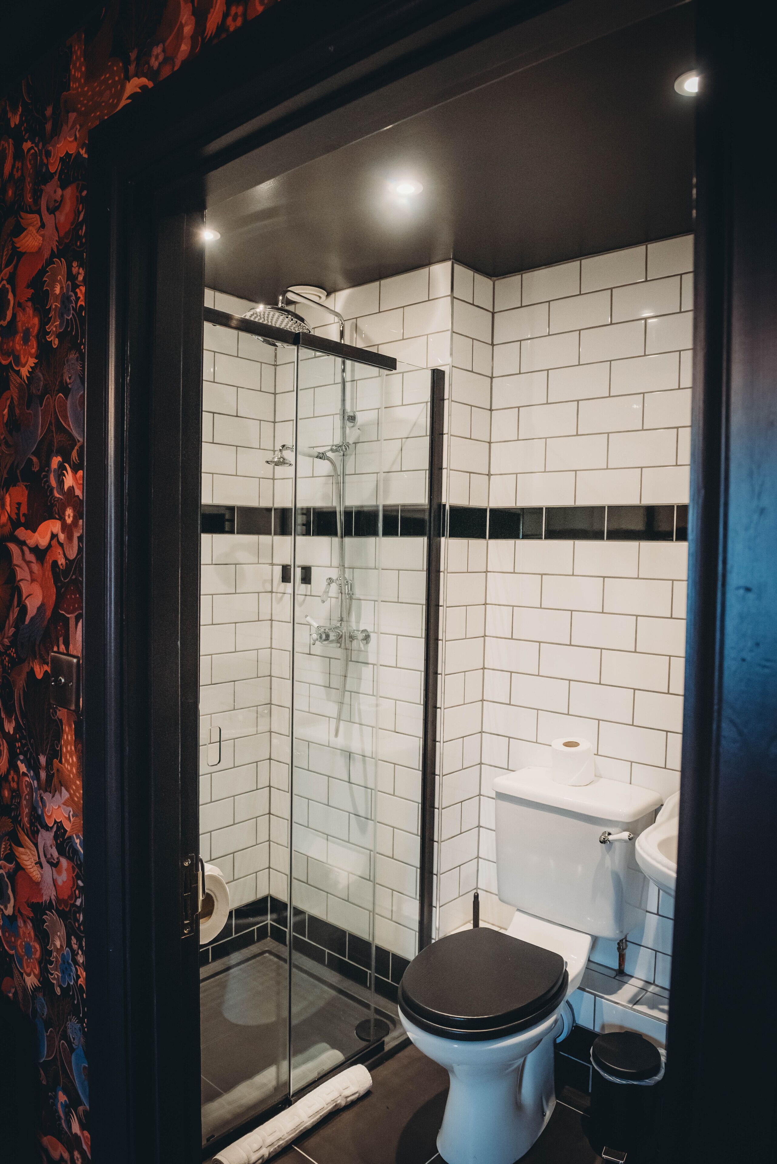 Een moderne badkamer met een douchekabinet van glas, witte betegelde wanden, een toilet en een wastafel.