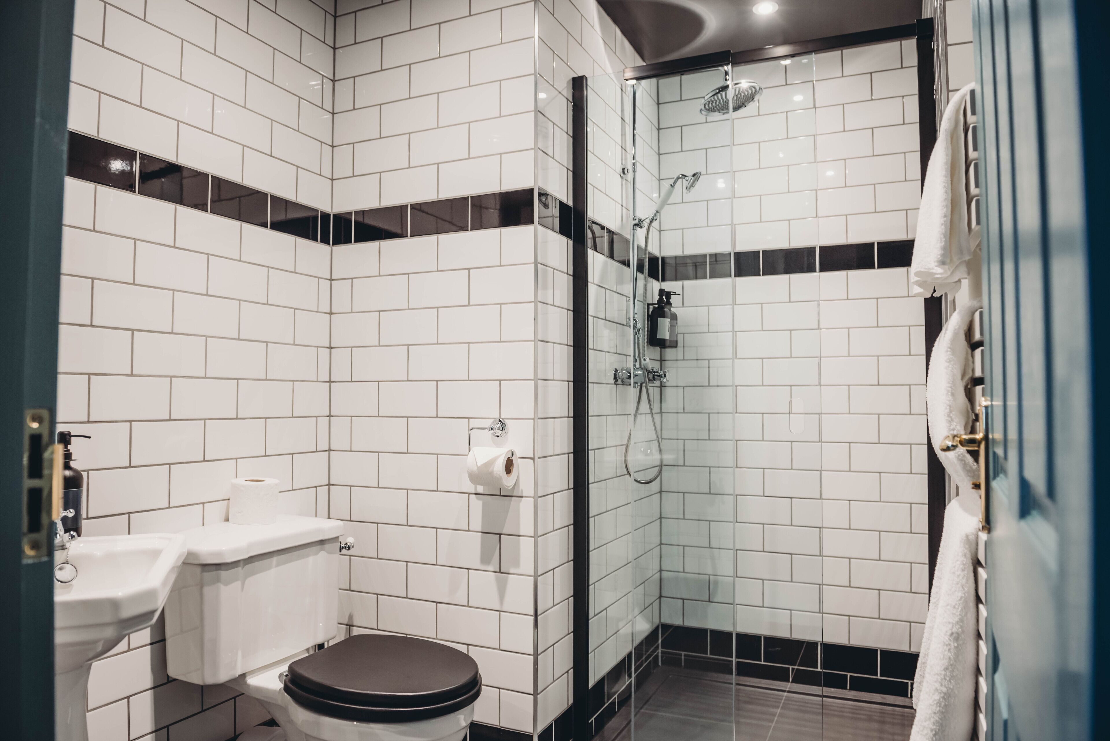 A bathroom with white tiled walls, a toilet, a sink, and a glass-enclosed shower area.