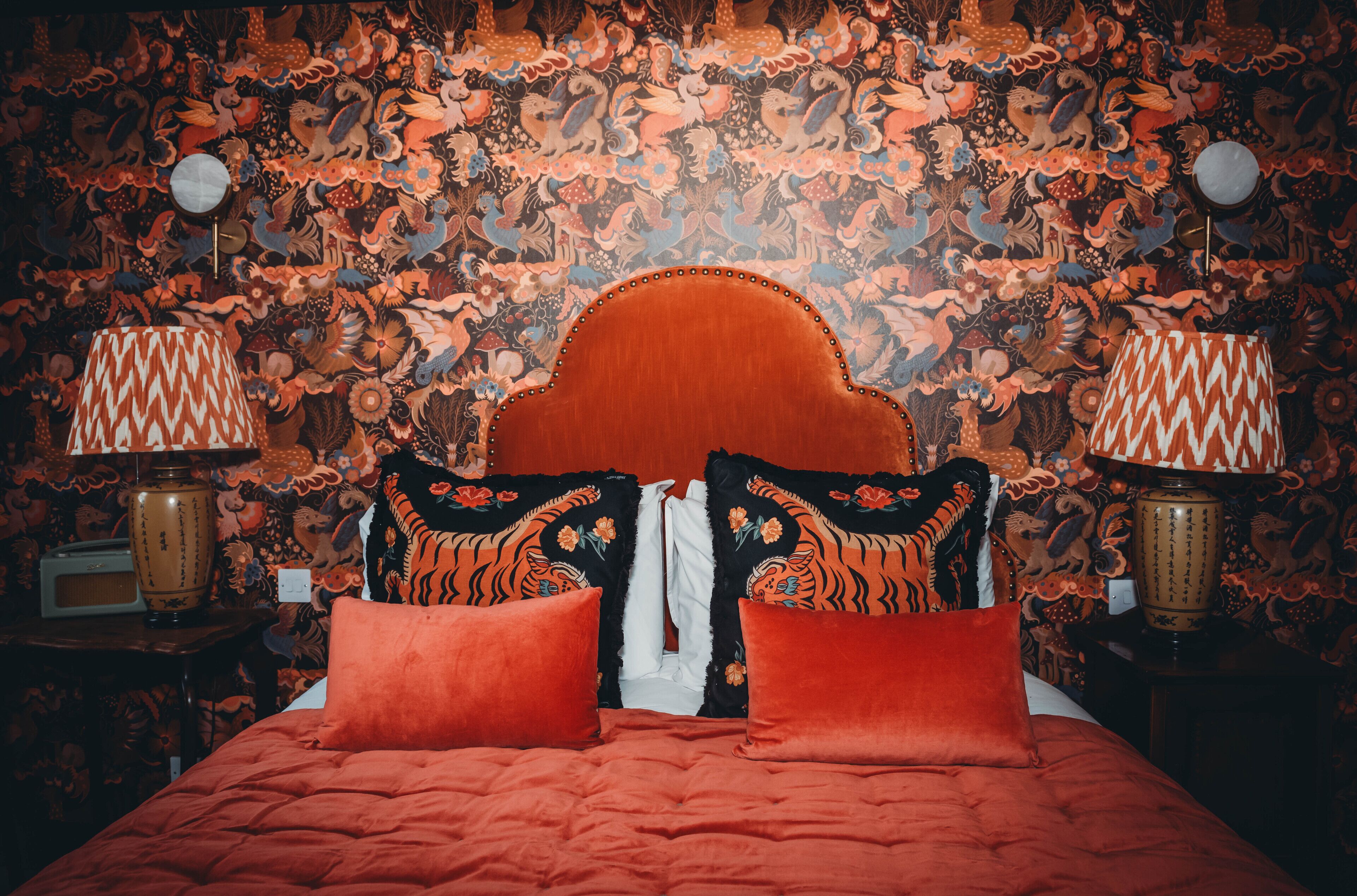 Un letto con testiera rossa e cuscini, una parete decorata con motivi e due comodini con lampade.