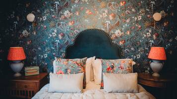 A bedroom with a floral wallpaper, a tufted headboard, a bed with white bedding, and two bedside lamps.