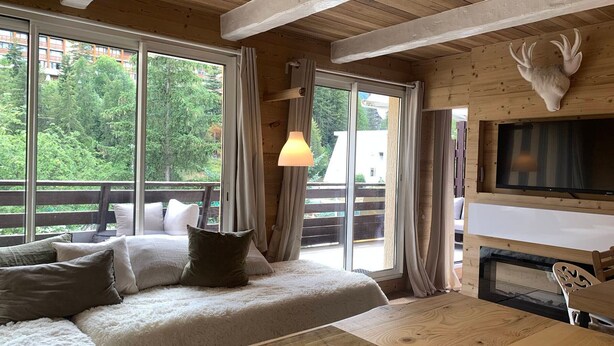 Una habitación acogedora con una cama grande, techo de madera, televisor montado y una decoración de cabeza de ciervo.