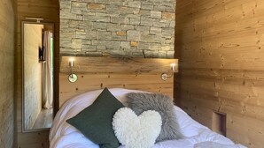 Un dormitorio con pared de piedra, paneles de madera, una cama con ropa de cama blanca y dos luces fijadas a la pared.