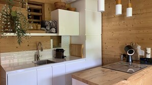 Una cocina moderna con armarios blancos, encimera de madera, lámparas colgantes y pared de madera rústica.