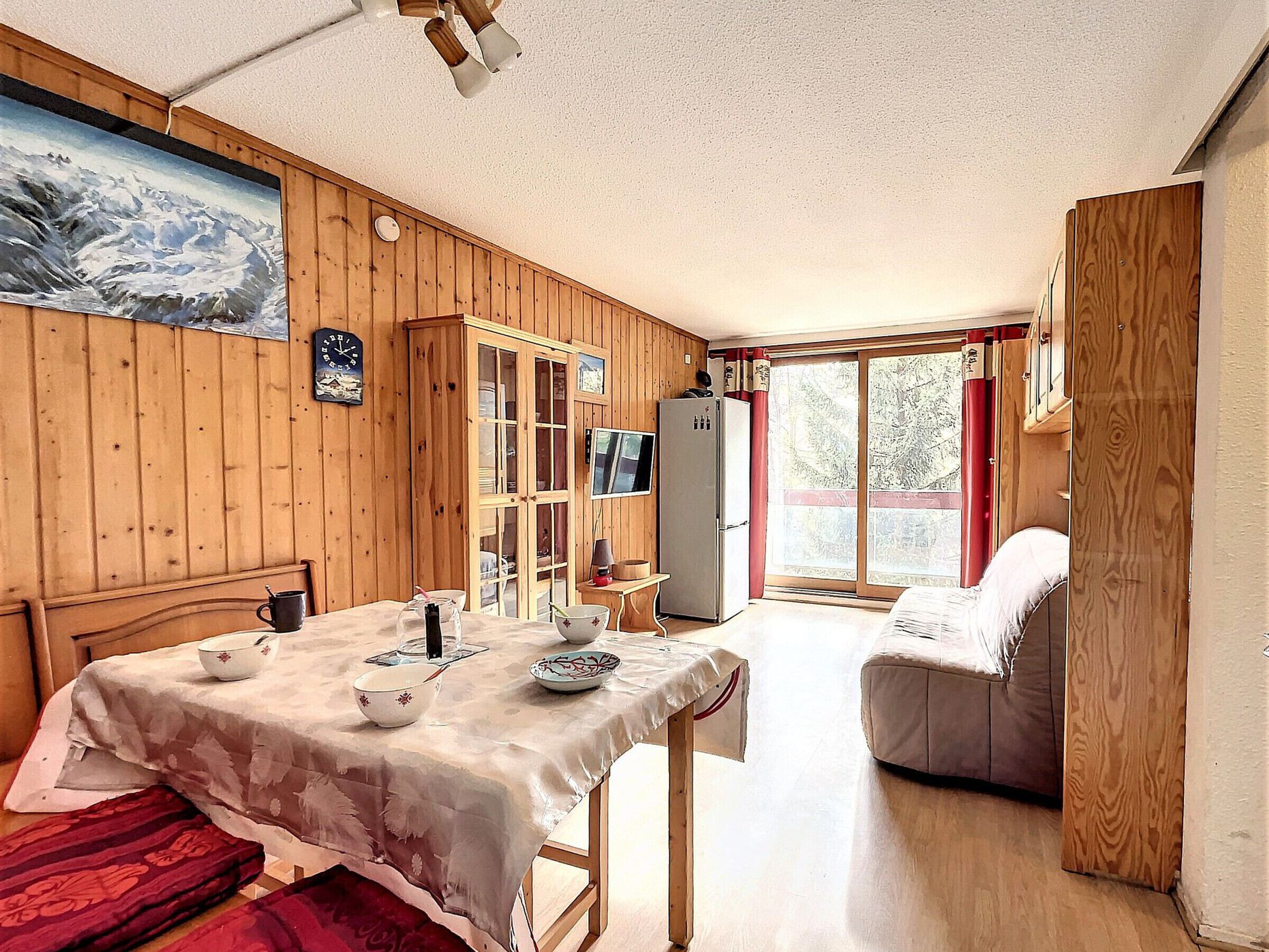 Una habitación acogedora con paredes de madera, una mesa de comedor con mantel, un sofá, un televisor y un refrigerador.