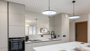 Una cocina moderna con una isla central, horno empotrado e iluminación colgante.