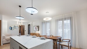 Una cocina moderna con una isla de mármol, una mesa de comedor de madera e iluminación colgante.