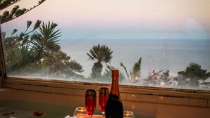 A table set with a bottle, glasses, and candles, overlooking a beach with palm trees and the sea. - Dream villa in San Felice Circeo (Faro)