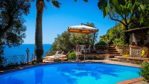 A clear blue swimming pool with a sun umbrella, lounge chairs, and a view of the sea. - Dream villa in San Felice Circeo (Faro)
